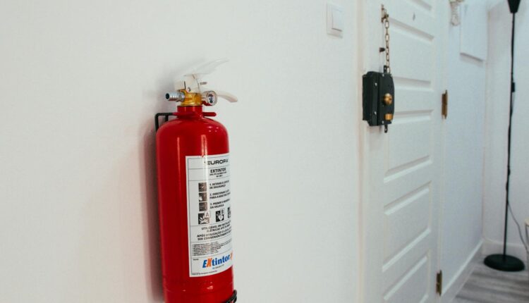 Red fire extinguisher mounted on a white wall in a modern apartment hallway.